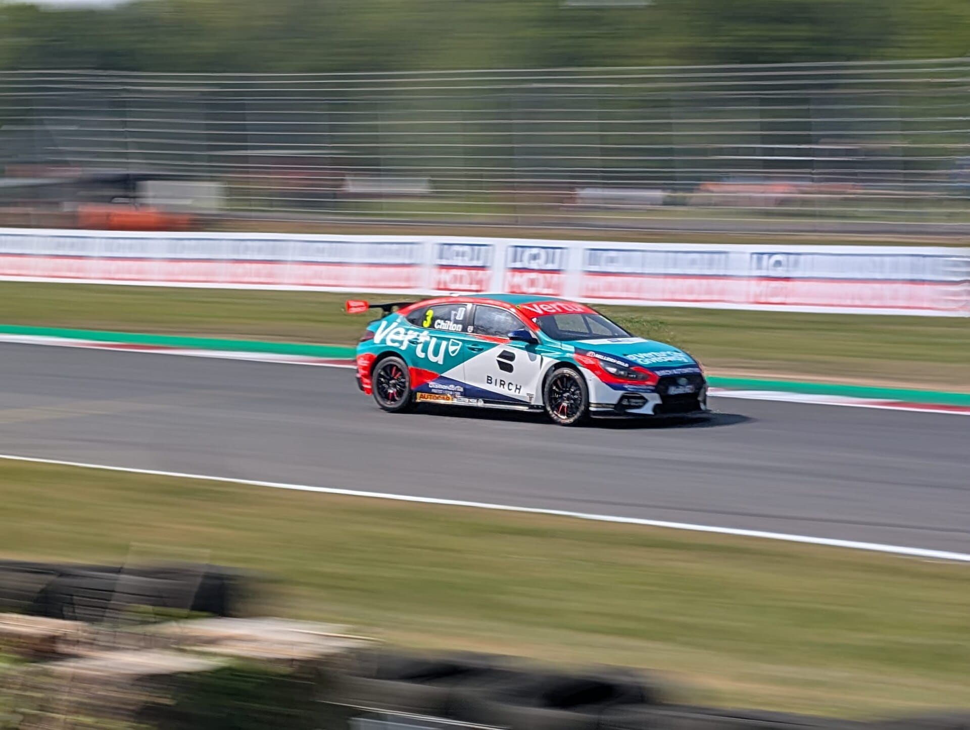 A British Touring Car Championship racing car speeding along a circuit track with motion blur on the background.