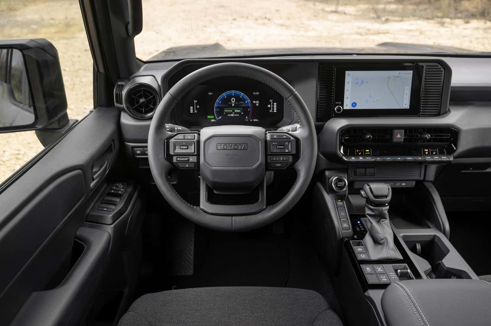 Interior view of a modern Toyota Land Cruiser 1958 trim showcasing the steering wheel with block TOYOTA text, digital cluster, center display, and dashboard controls.