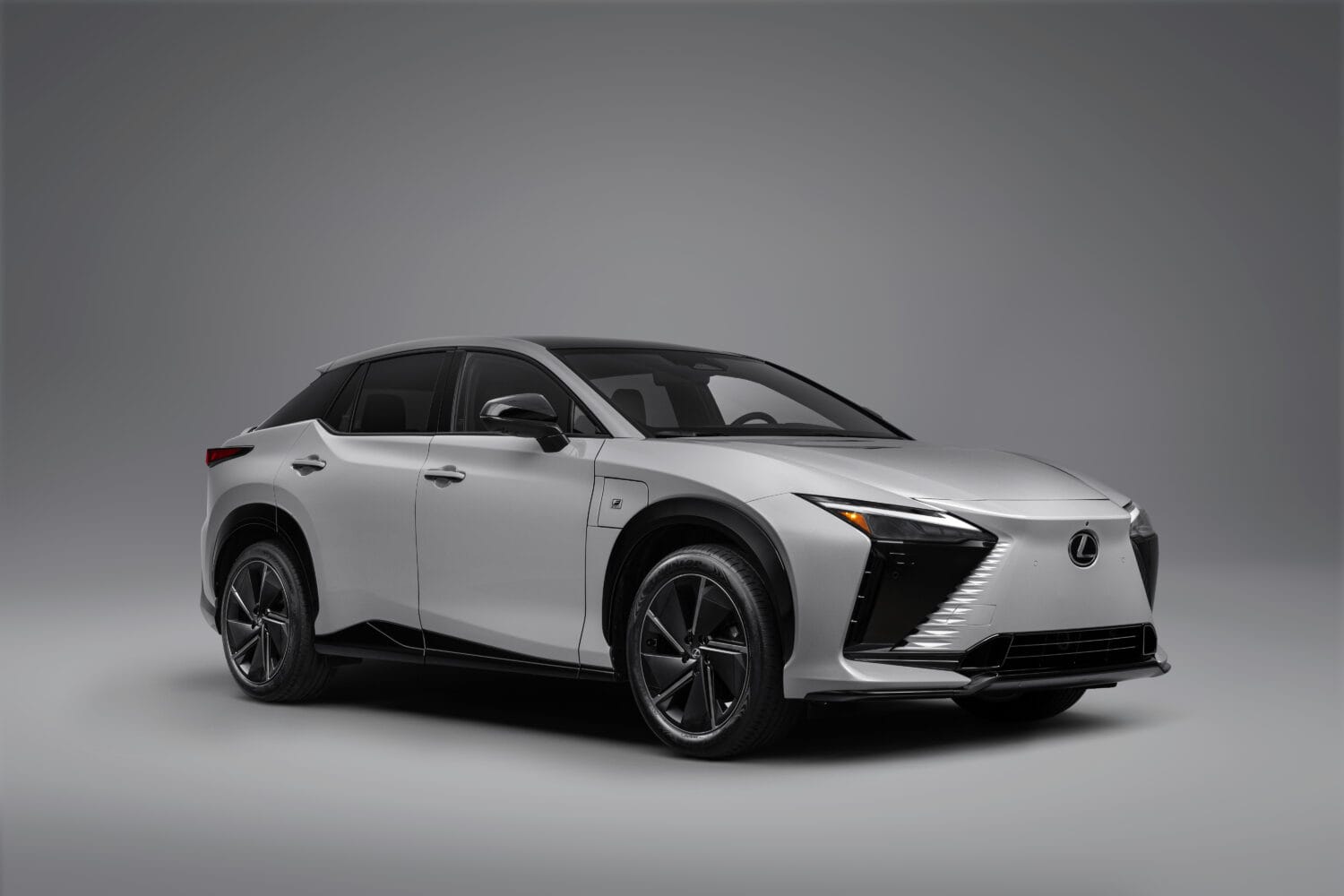 Studio shot of a silver Lexus electric SUV viewed from the front three-quarters angle against a plain gray background.