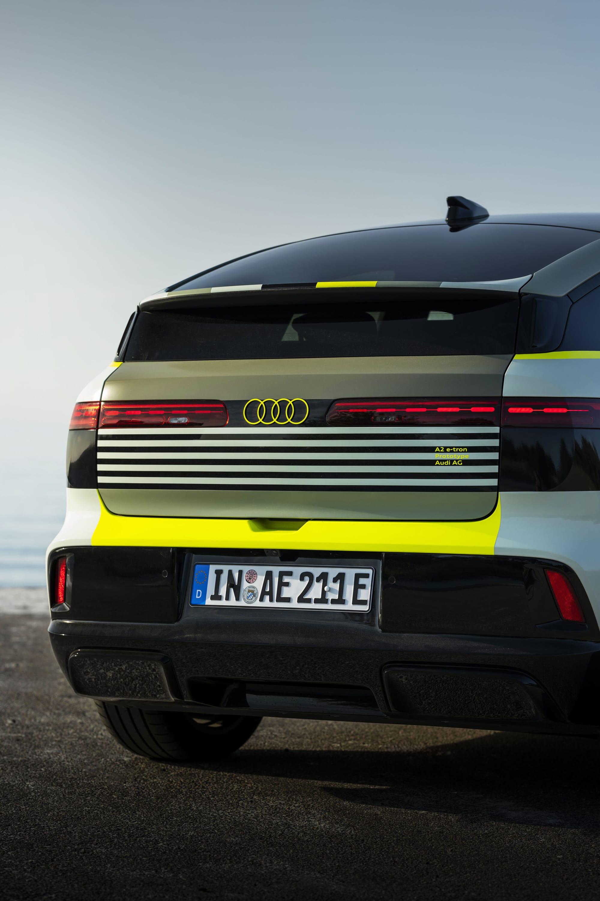 Close-up rear view of the Audi A2 e-tron prototype vehicle parked outdoors, showing the tailgate, distinctive LED taillights, Audi four-rings logo, license plate, and yellow accent stripes.