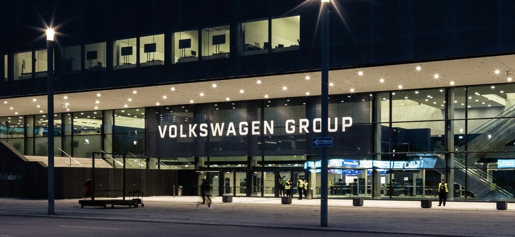 An exterior view of a modern building at night featuring the text 'VOLKSWAGEN GROUP' prominently displayed over the entrance.