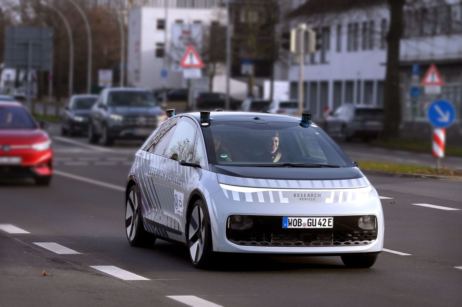 A silver Volkswagen research vehicle driving on a city street, equipped with sensors on the roof and special graphics on the body.