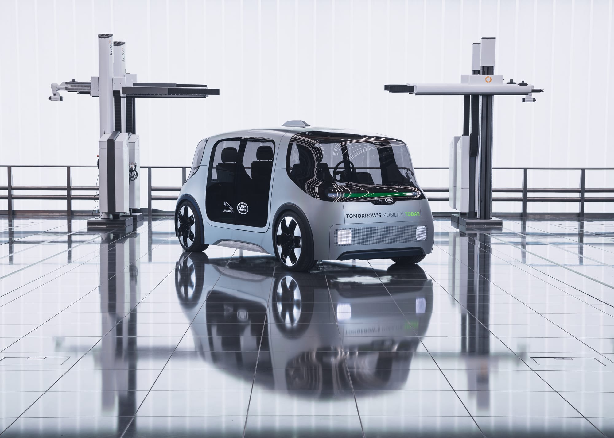 A futuristic autonomous concept vehicle by Jaguar Land Rover parked on a reflective studio floor between robotic measuring equipment, displaying the Jaguar and Land Rover branding on its side and front.