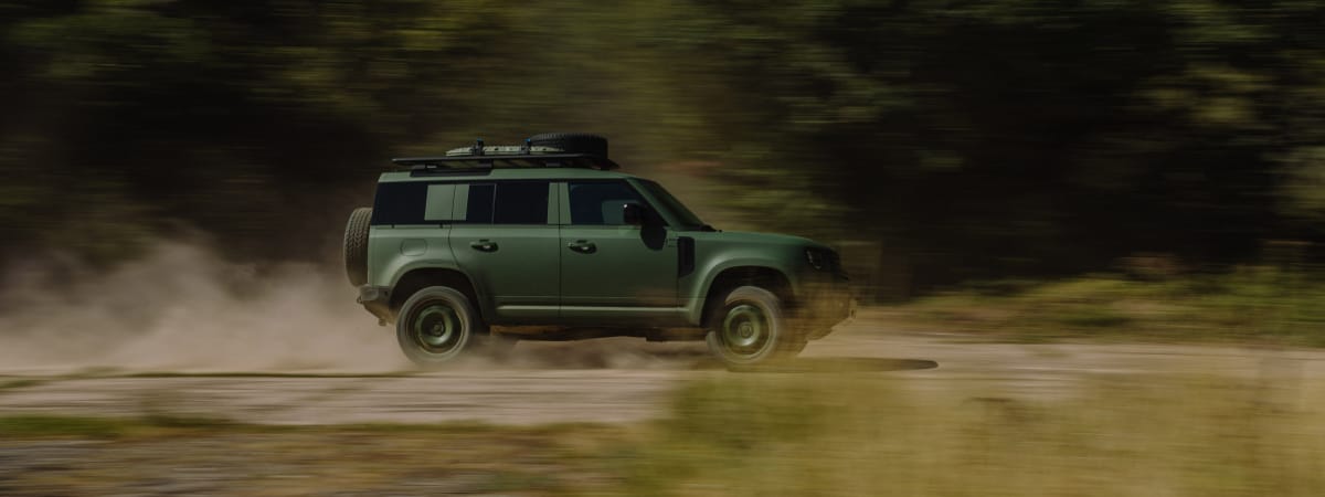 A green off-road vehicle driving fast on a dirt track, kicking up dust with motion blur background.