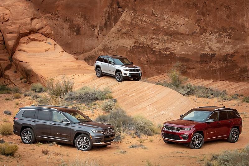 Three Jeep Grand Cherokee SUVs parked in a rocky desert landscape with red rock formations.