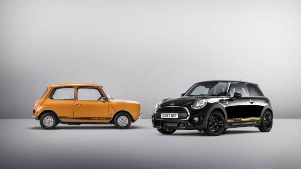 Studio photograph showing a classic orange Mini Cooper alongside a modern black Mini Cooper against a gradient gray background.