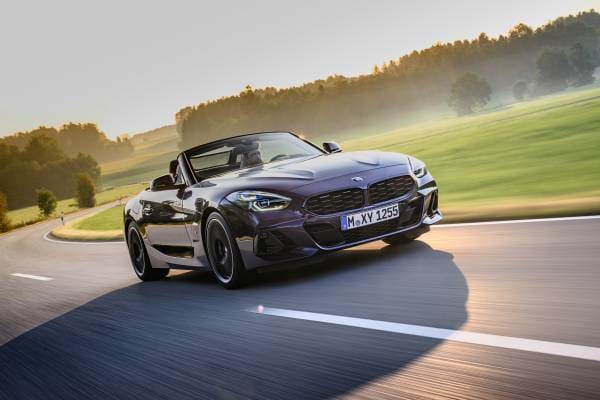 A sleek dark convertible BMW Z4 driving along a scenic country road during sunset with motion blur on the pavement.