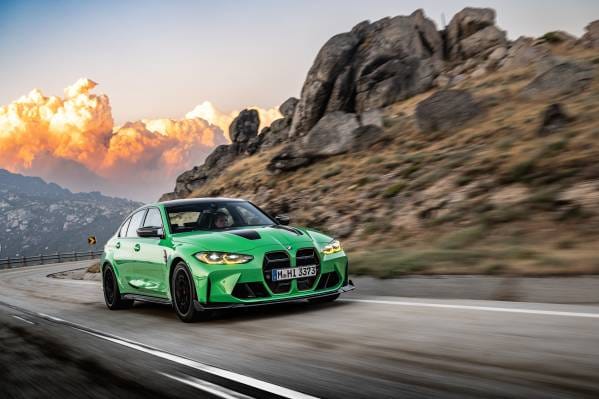 A green BMW M3 driving along a winding mountain road during sunset.