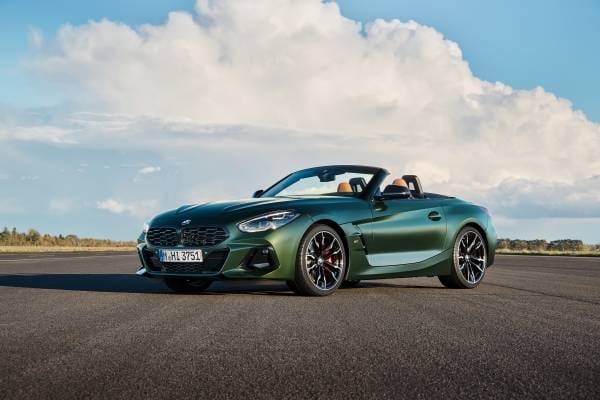 A dark green BMW Z4 convertible parked on an asphalt surface under a cloudy sky.