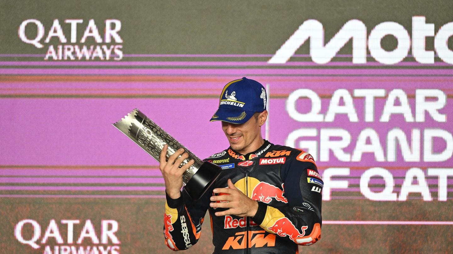A medium shot of Maverick Viñales holding a trophy on a podium against a branded background with Qatar Airways and MotoGP logos.