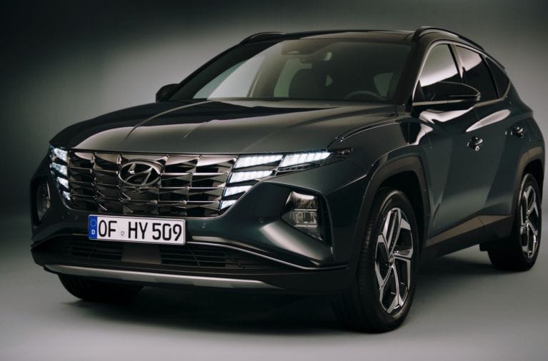 Studio shot of a dark green Hyundai Tucson SUV from a front three-quarters angle, featuring distinctive LED headlights integrated into the grille and a German license plate.
