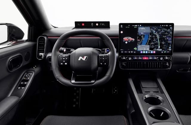 An interior shot of a car dashboard, showcasing the steering wheel and the Pleos Infotainment System display screen.