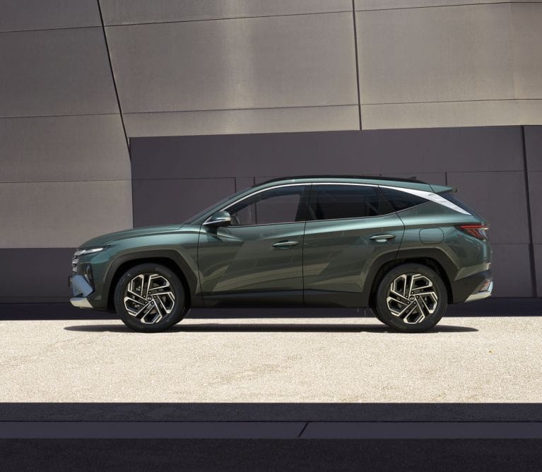 A side profile view of a green Hyundai Tucson parked outdoors against a modern architectural background.