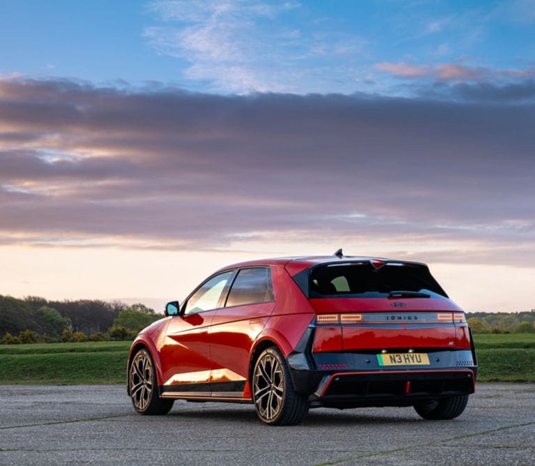 A red Hyundai Ioniq 5 parked on asphalt against a sunset sky.