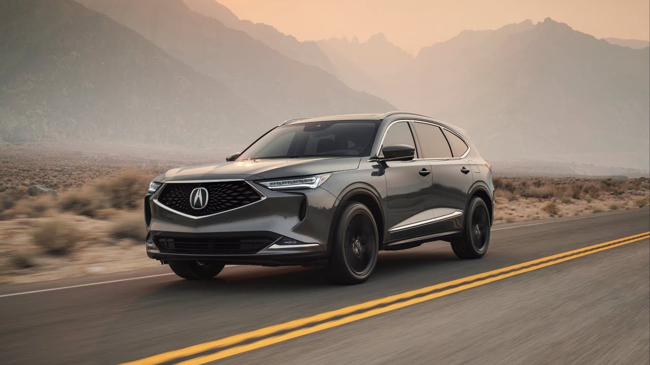 A grey Acura SUV driving along an open highway with majestic mountains in the hazy background during dusk.