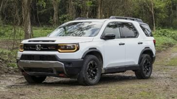 A white Honda Passport TrailSport SUV parked on a dirt trail surrounded by green trees and foliage.