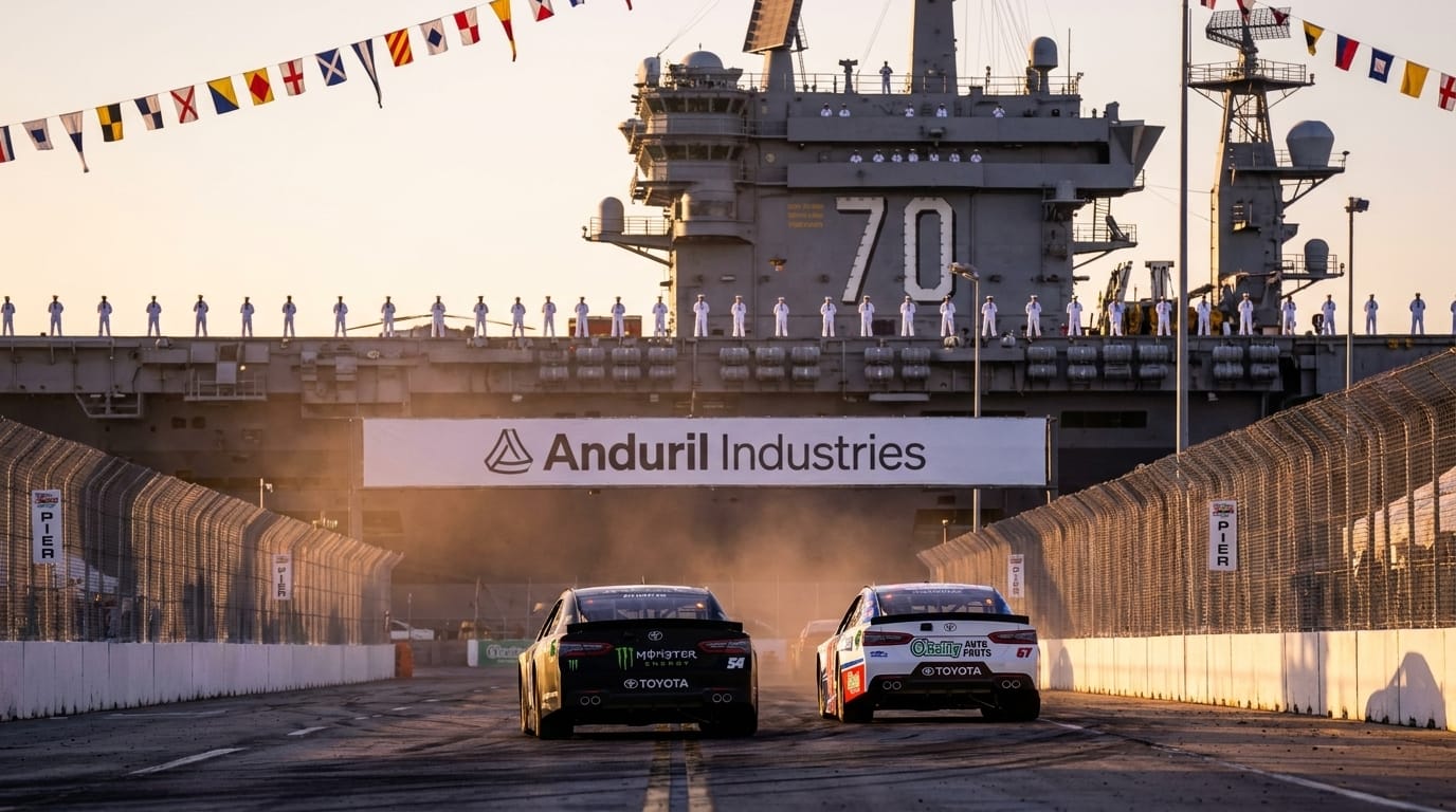 Bakifrånfoto av två stock race-bilar som kör sida vid sida på en bana bredvid ett hangarfartyg i solnedgång.