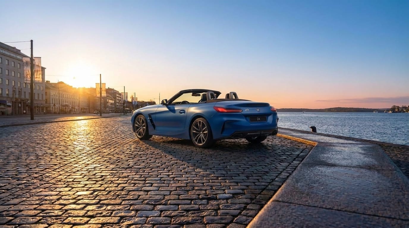 Blå BMW Z4 roadster parkerad på kullerstensgata vid vatten i solnedgång.