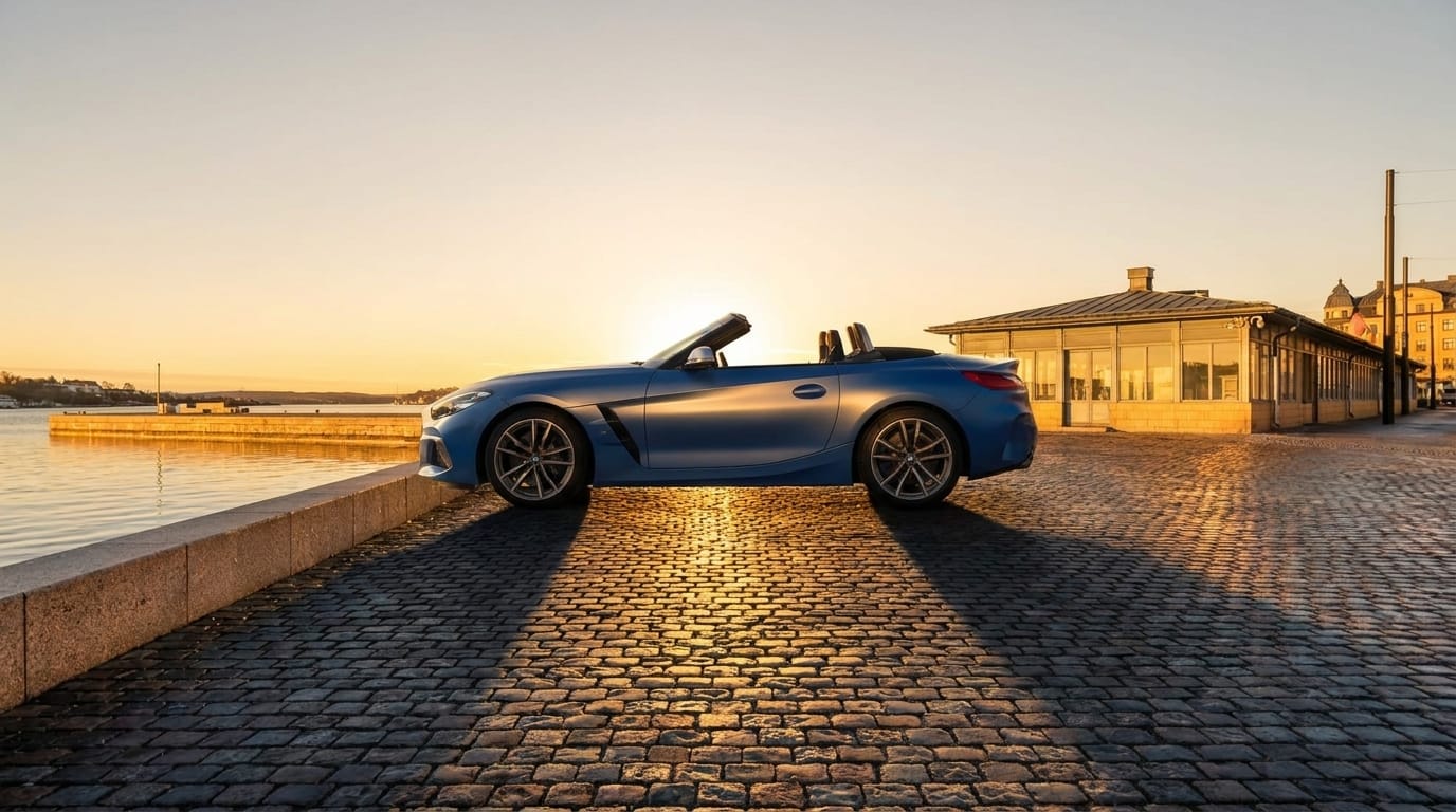 En blå cabriolet parkerad på kullerstensbelagd kaj i solnedgång.