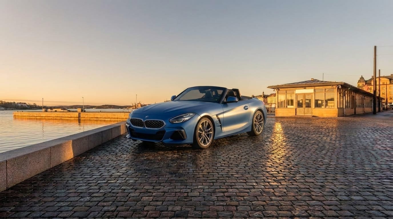 En blå BMW Z4 står parkerad på kullerstensbelagd kaj vid vattnet i solnedgång.