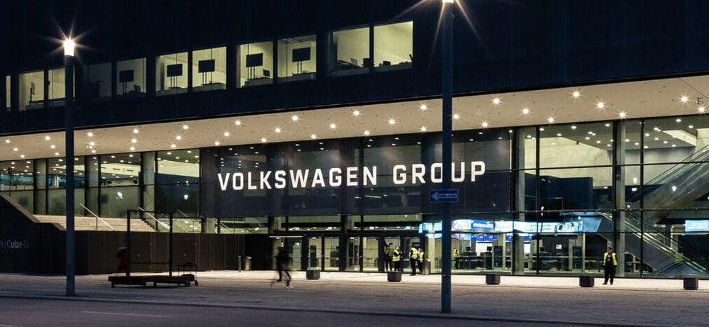 An exterior view of a modern building at night featuring the text 'VOLKSWAGEN GROUP' prominently displayed over the entrance.