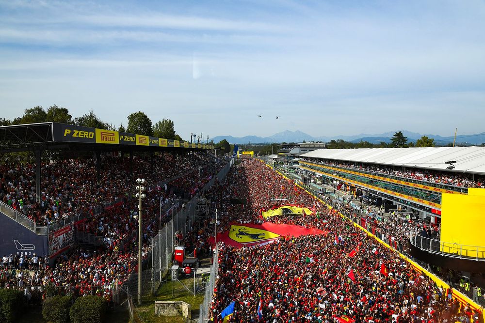 A high-angle wide establishing shot of the Italian Grand Prix at Monza, showing a massive crowd of fans filling the racetrack and grandstands with flags and banners.