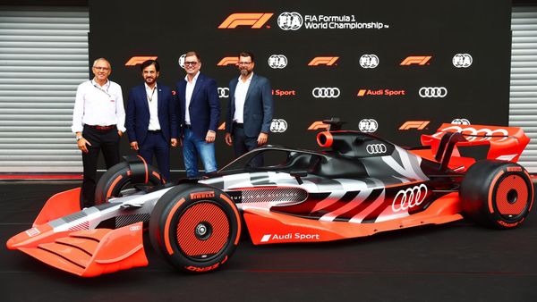 Four executives standing behind an Audi Formula 1 concept car against a black FIA Formula 1 World Championship backdrop.