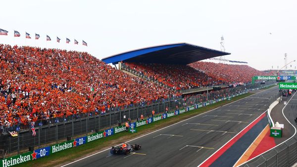 Wide shot of a Red Bull Formula 1 car driving along a racetrack in front of grandstands packed with orange-clad spectators.