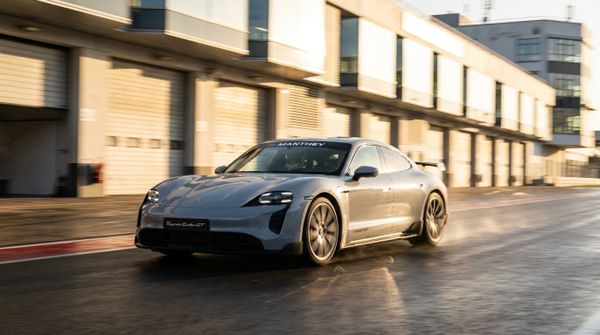 En silvergrå Porsche Taycan Turbo GT kör snabbt längs Nürburgrings depågata i ett varmt gyllene kvällsljus.