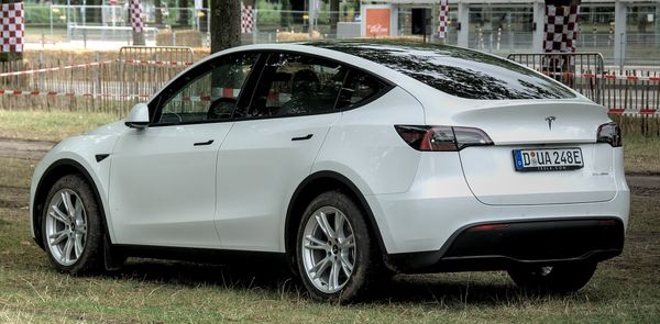A white Tesla Model Y parked outdoors with a rear three-quarter view, showing its sleek design and branding.