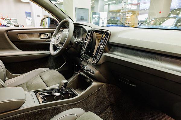An eye-level interior view of a modern Volvo car dashboard, steering wheel, and front seats inside a showroom.