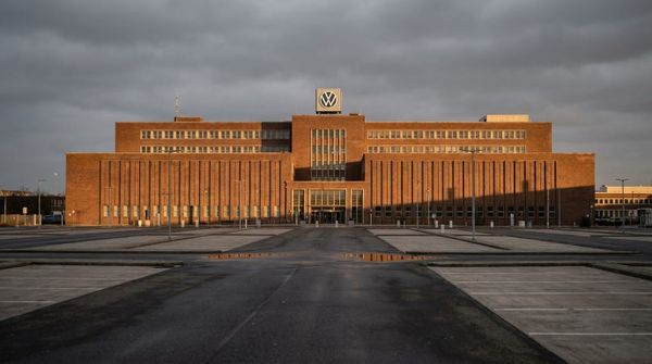 Den monumentalna exteriören av Volkswagens huvudkontor i Wolfsburg under en mulen himmel med en tom parkeringsplats i förgrunden.