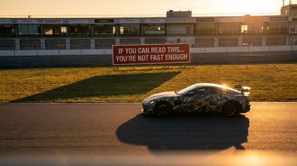 En bil med kamouflagefärg står parkerad på en racerana vid solnedgången med långa skuggor.