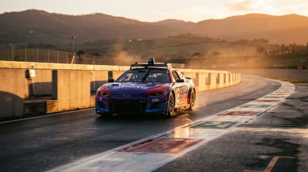 En autonom racingbil kör genom en kurva på en italiensk racerbana i gyllene solnedgångsljus.
