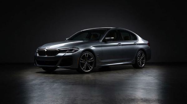 En grå BMW M550i xDrive står parkerad i en mörk studio med polerat betonggolv.
