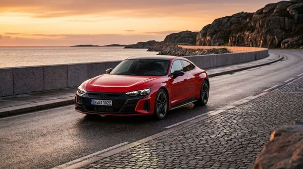 Röd Audi e-tron GT kör längs en kustväg i solnedgången.