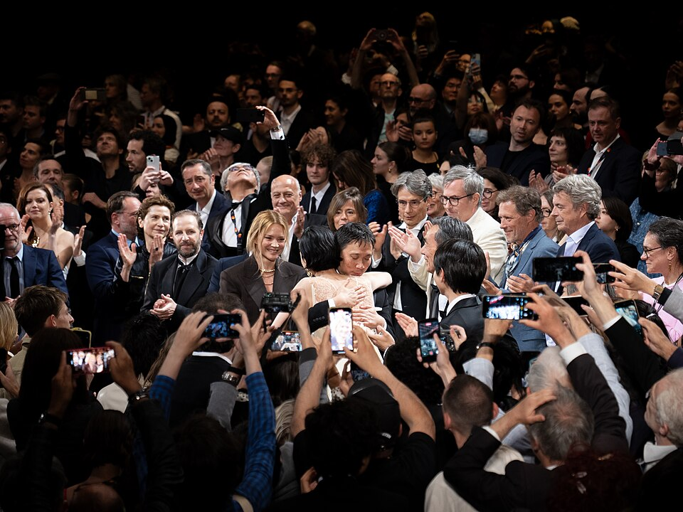 Japanese director Ryusuke Hamaguchi hugs Japanese actress Tao Okamoto during the standing ovation for their film All Of A Sudden at 2026 Cannes Film Festival. By FireBirdFilm / WikiPortraits, CC BY-SA 4.0, https://commons.wikimedia.org/w/index.php?curid=192106310