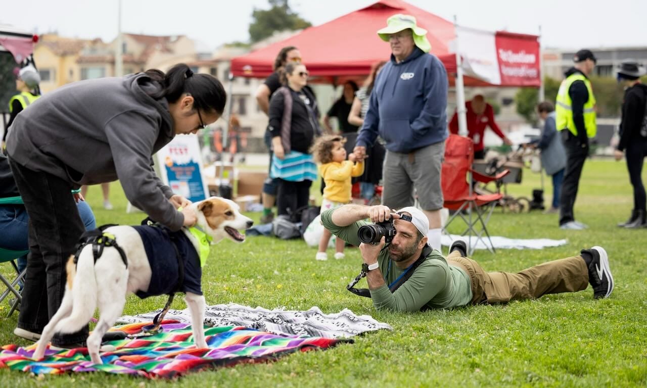 A WikiPortraits photographer lying on the grass to photograph a dog at an outdoor community event