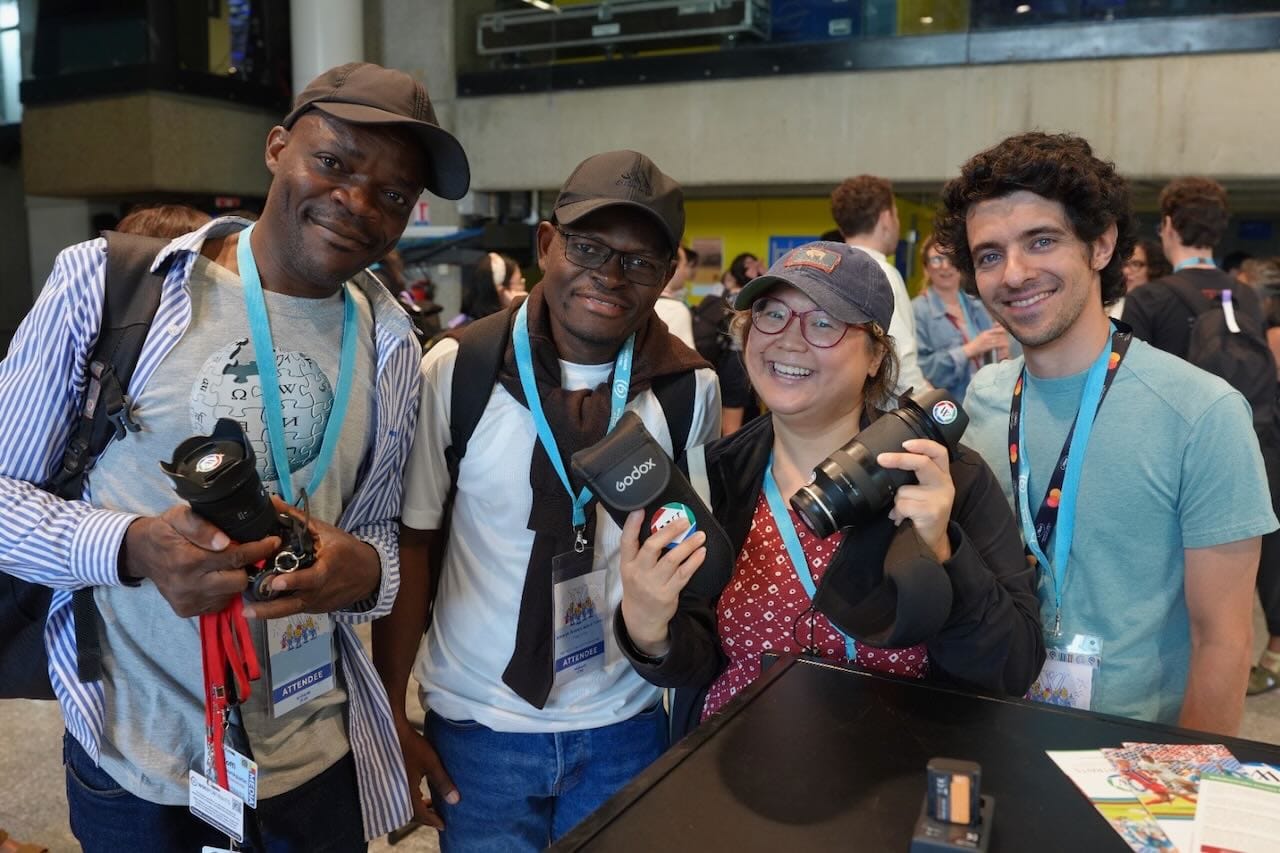 Four WikiPortraits photographers holding cameras and lanyards, smiling together at a Wikimedia event