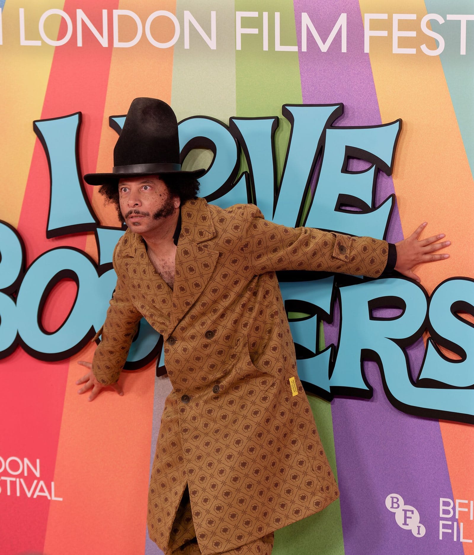 Boots Riley in a patterned coat and tall black hat in front of the colorful I Love Boosters backdrop