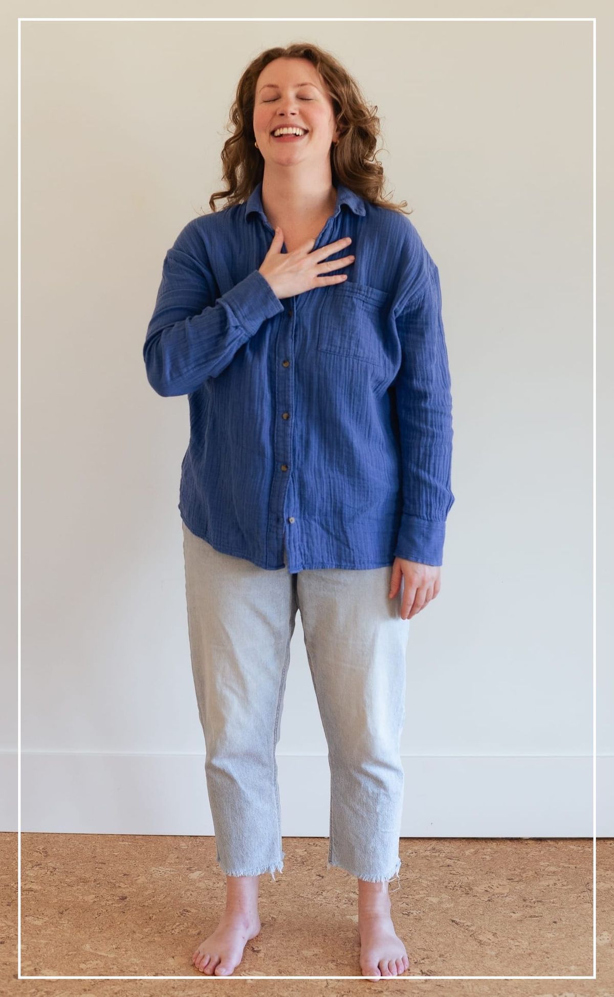 a white woman stands in blue shirt stands barefoot in a room, with her right palm placed over her heart
