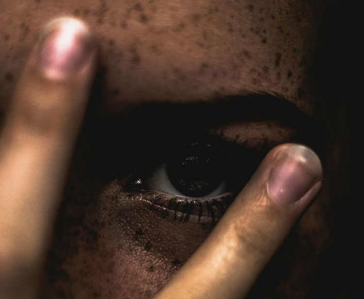 A person covering their face with their fingers, zoomed in on the left eye.