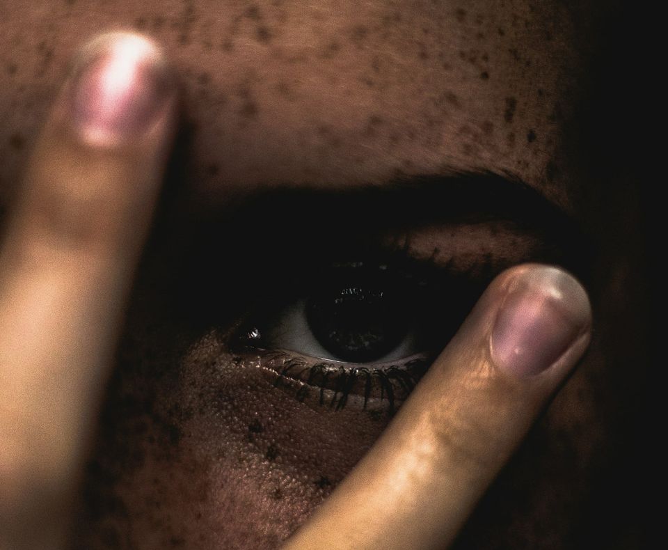 A person covering their face with their fingers, zoomed in on the left eye.