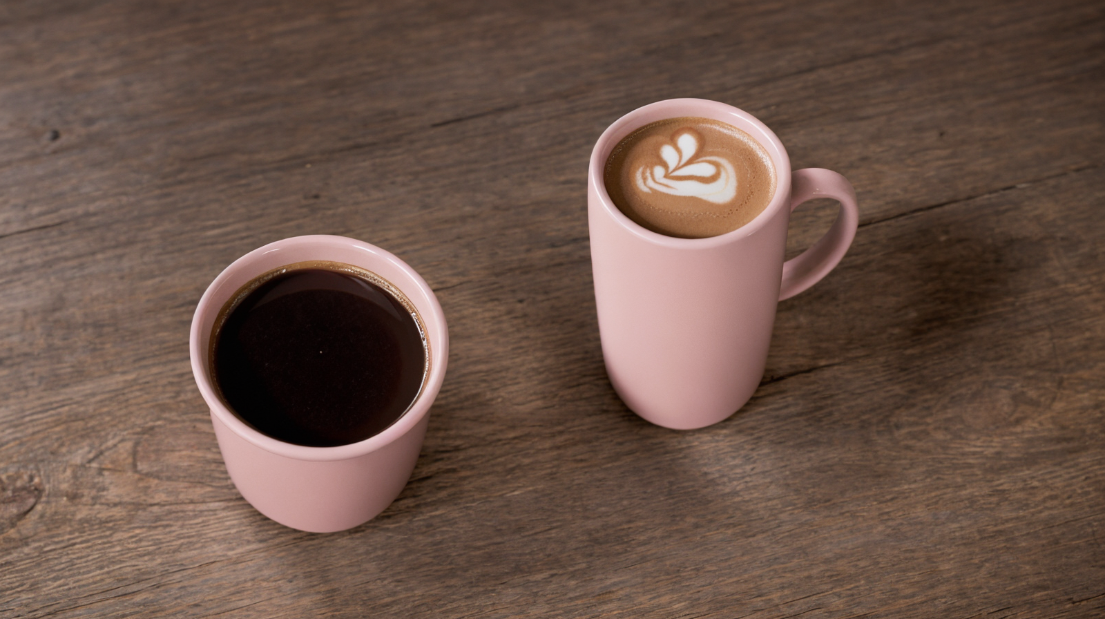 Photorealistic product style photography of two pink ceramic coffee mugs on a wooden surface, generated with Realistic Vision on Eachlabs.