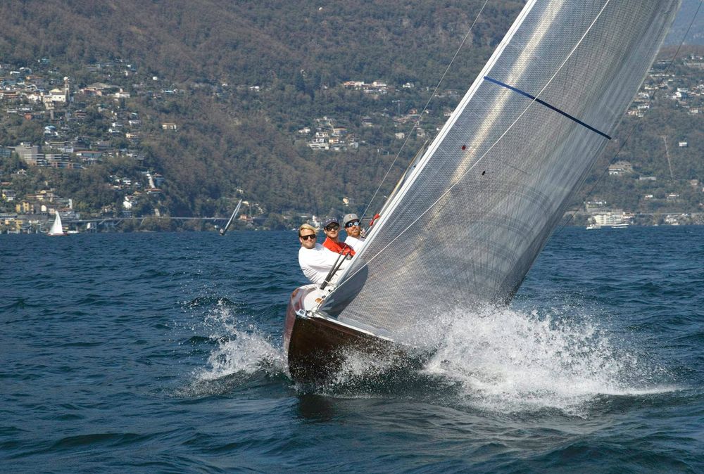 Racing monohull heeling hard with crew on the rail, water spraying from the bow