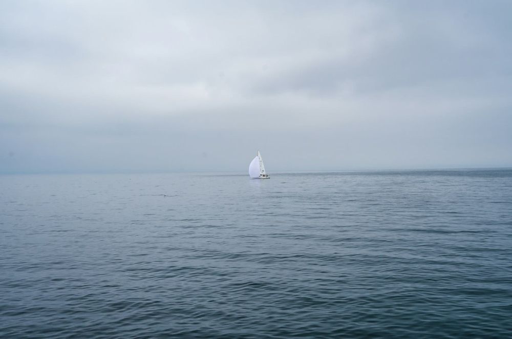 Lone sailboat reduced to deeply reefed sail in heavy fog and overcast