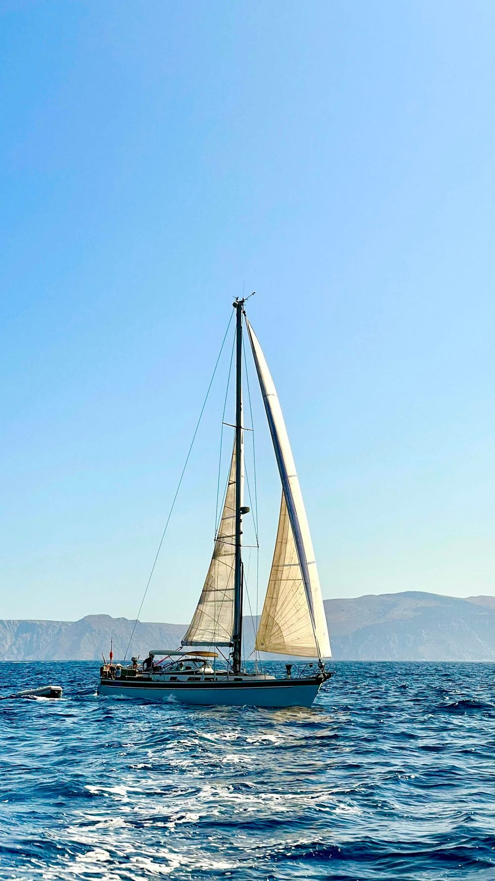 Cruising sloop close-reaching offshore with mountains on the horizon