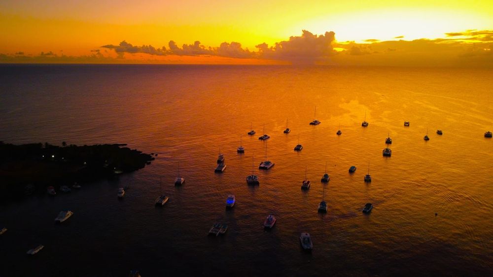 Catamarans and sailboats anchored in a tropical bay at sunset, viewed from above