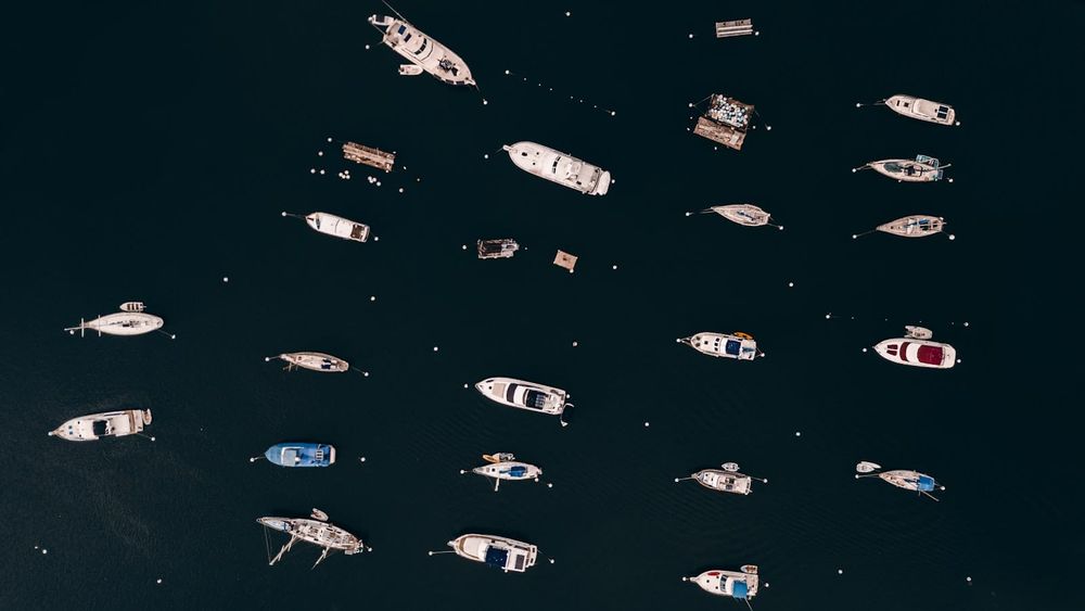 Aerial view of a busy mooring field with dozens of cruising boats anchored on dark water