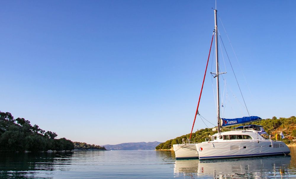 A bluewater catamaran lying at anchor in clear tropical water, viewed from astern.